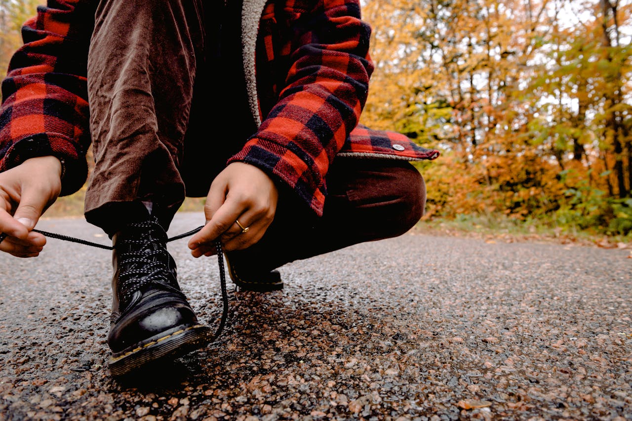 Close-up of a person tying boots on a road surrounded by fall foliage.